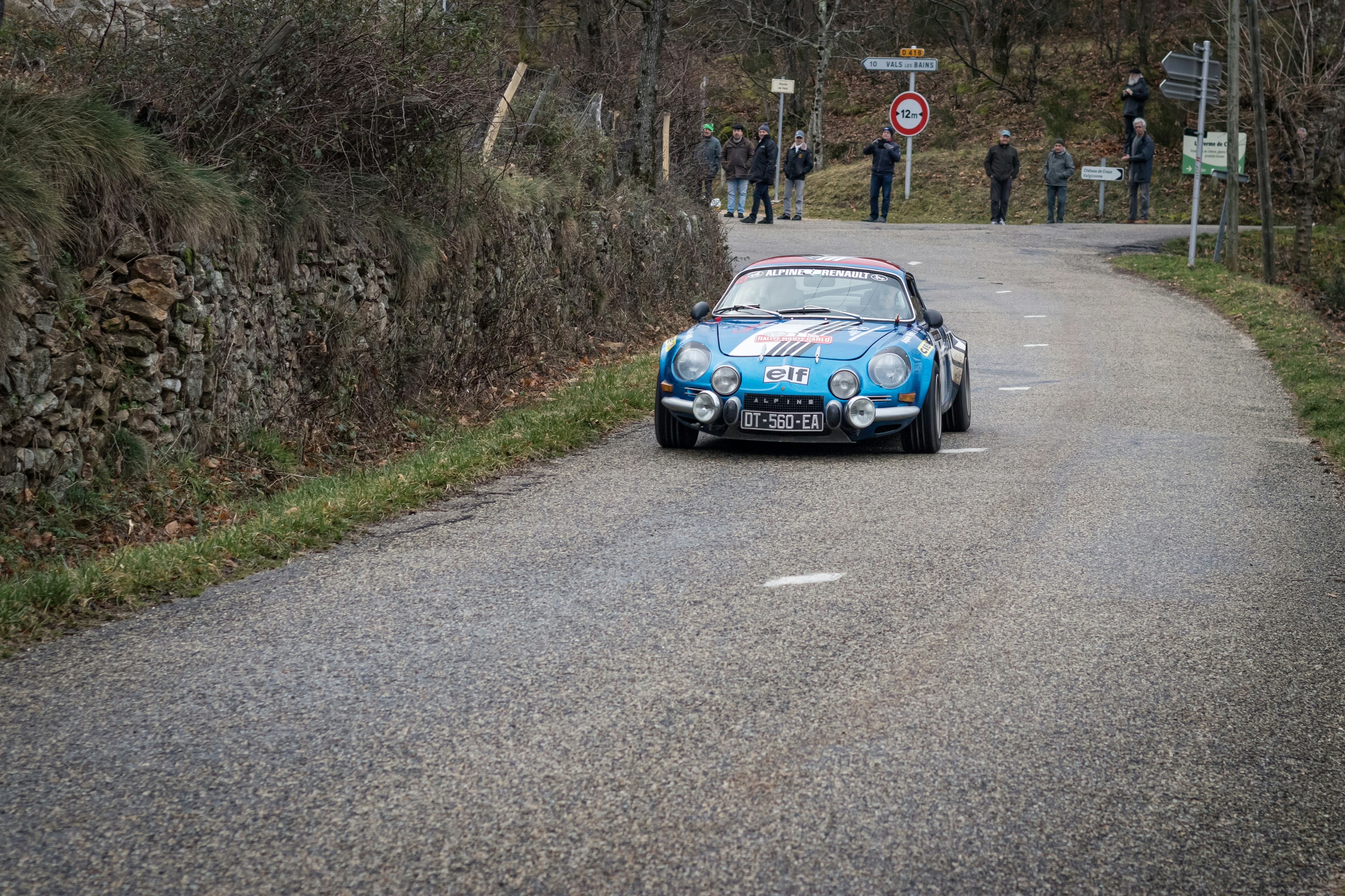 A vintage blue car driving down a road.