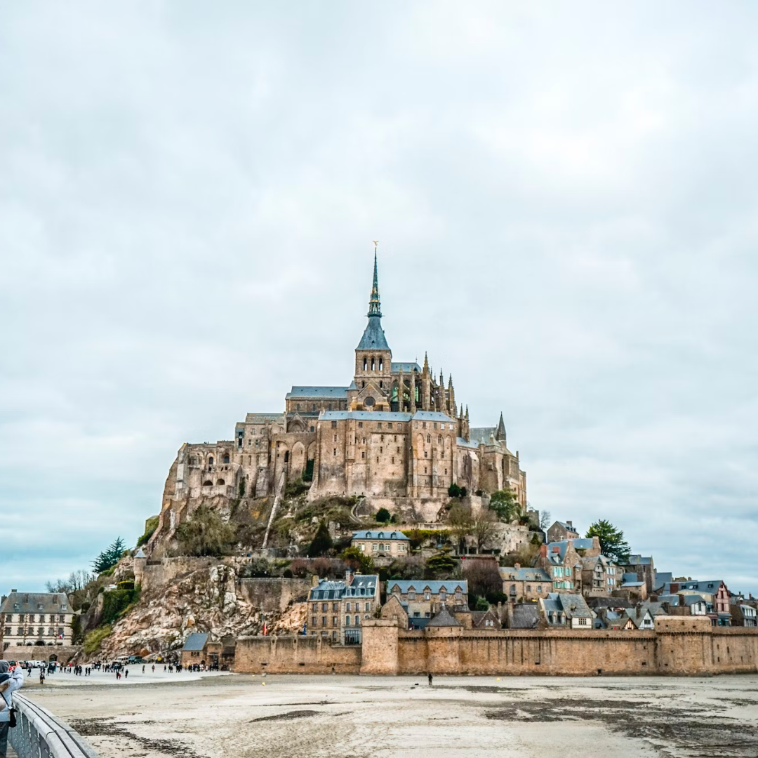 An image of Mont Saint Michel, a village looking island with a castle in the middle and causeway through the water leading to it.