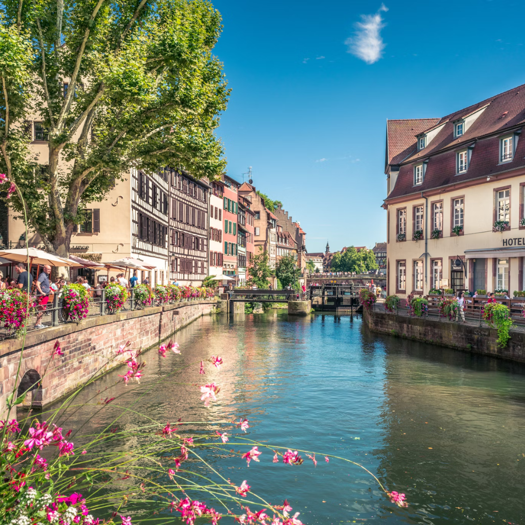 A river running through the city of Strasbourg with restaurants and older style hotels on either side.