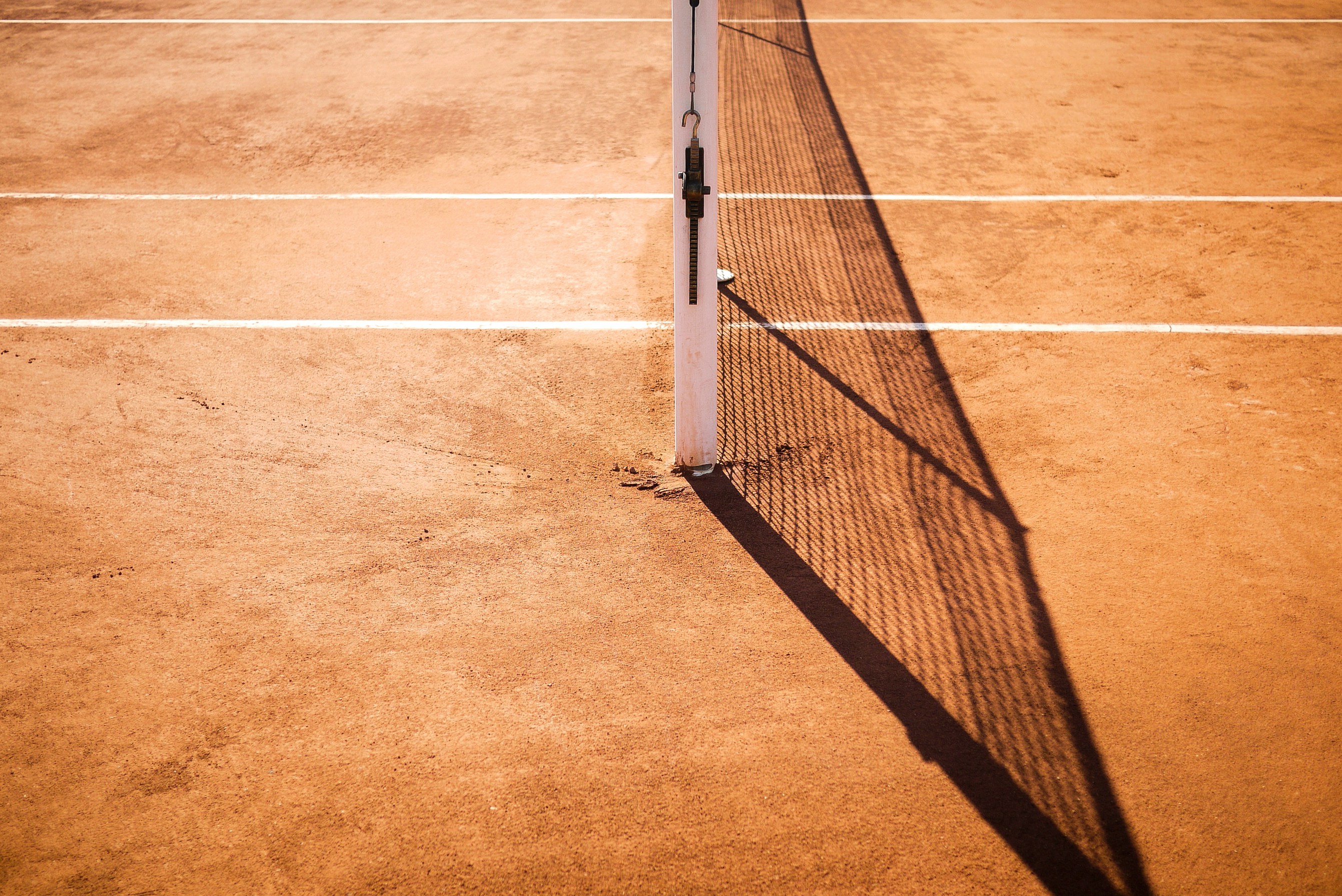 An image of a brown clay/sandy tennis court zoomed in to the side of the net.